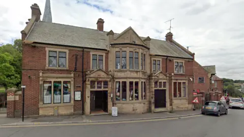 Google A large two-storey brick pub with Chesterfield's twisted church spire in the background