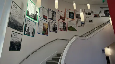 Debbie Graham A curved staircase with lots of pictures on the wall telling the story of Seker fabrics.