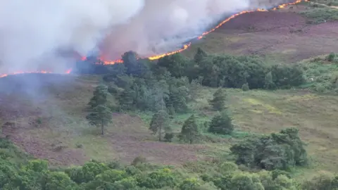 Stunning Drone Orange and red flames in the trees and white smoke flowing up into the sky can be seen for several miles.