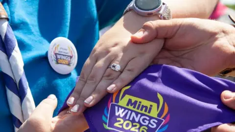 TINA WING The picture shows a hand with a engagement ring that is based on the Scout membership badge and the knot style that features on it and a diamond on top