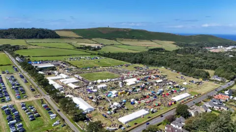 CJS PHOTOGRAPHY The show field from above. It shows people milling around a series of white marquees, stock judging pens and arenas; cars are parked to one side.