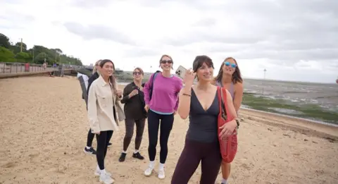 Connor Bennett/BBC A small group of women, many with sunglasses, standing on a beach