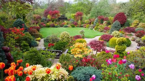 Four Seasons Garden A lush green garden surrounded by an array of colourful flowers and foliage.