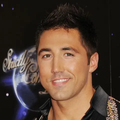 Getty Images Gavin Henson on Strictly Come Dancing. He looks at the camera and smiles. He has a black shirt on with sequins around the collar and has his gelled hair. Behind him is a Strictly logo.