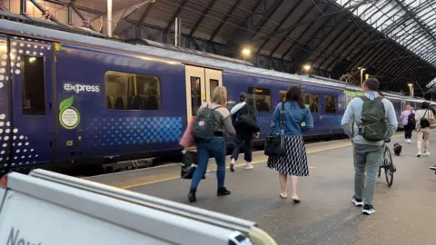 People walk along a platform to board a ScotRail train