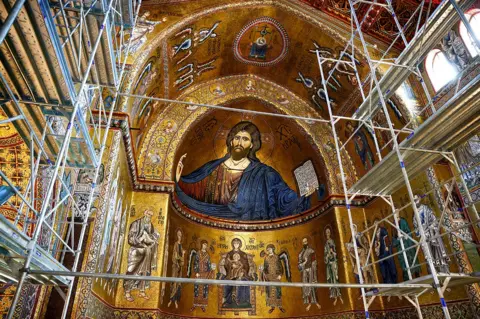 Reuters Bagian atas katedral Monreale di Sisilia, menunjukkan detail mosaik Kristus dan simbologi agama lainnya yang sebagian besar terbuat dari emas, dengan perancah di latar depan. 