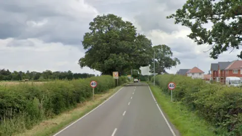 Google Bosworth Lane, between the A447 and Newbold Verdon in Leicestershire, featuring greenery and 40mph signs on both sides of the road. There are also some houses to the right and a field to the left with trees after road signs.
