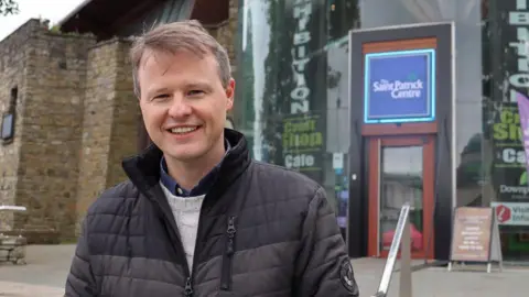 Chris Buckler in a padded grey jacket and grey knitted sweater. He has short brown hair.