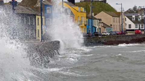 Large waves crashing over the promenade at Donaghadee. Colourful terraced buildings are along the seaside.