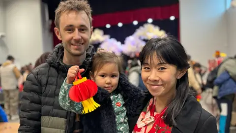 A man and a woman holding their daughter, who has made a paper lantern.