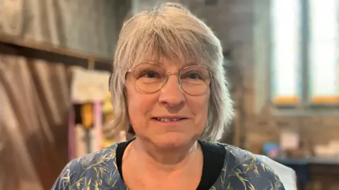 A woman in a church smiles at the camera wearign a blue and white dress