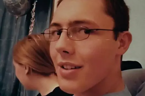 BBC Scotland A close-up shot of Aaron Sawn, who has dark hair and is wearing metal-rimmed glasses. 