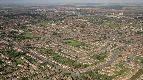 Aerial view of Scunthorpe showing rows of houses and parks with the steel works in the background