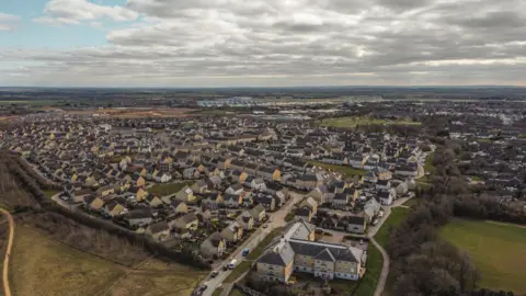 A bird's eye view of Carterton, with countryside around the edges. The land is flat and the sky is generally cloudy