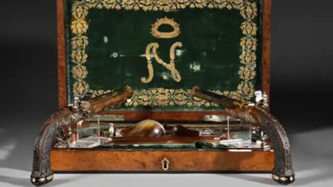 Two pistols stand in front of a wooden box