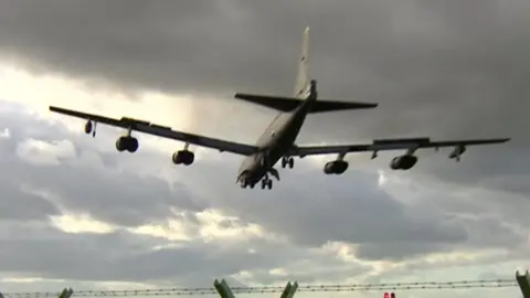 An archive image of a B-52H bomber coming in to land at RAF Fairford. The airfield is bordered by barbed wire. 