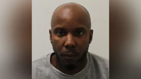 A mugshot of Owusu in a grey crewneck shirt. He stares blankly at the camera.