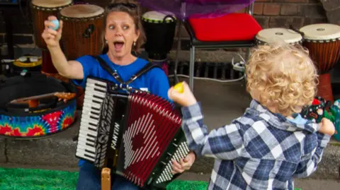 A charity team member plays an instrument with a child who has blonde, curly hair