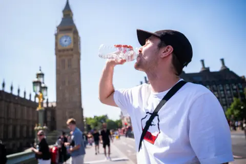 PA Media A man in a white t-shirt and black cap cools down with a bottle of water during the hot weather in Westminster Bridge, central London. 