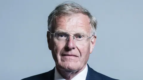 UK Gov Official photo of Christopher Chope who is not smiling and is wearing silver-rimmed glasses