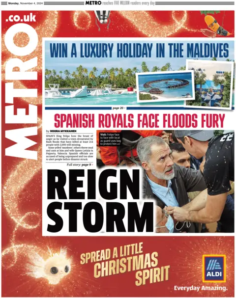 Primeira página do jornal Metro. A manchete diz: “Reign Storm” com uma foto do rei Felipe da Espanha cercado por pessoas, segurando a mão de um morador local. Ambos têm lama nas roupas e no rosto.