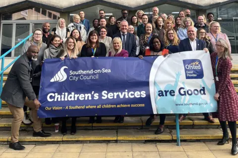 Southend-on-Sea City Council About 40 people are standing on steps outside Southend-on-Sea City Council's offices.  The people at the front are holding a banner, which reads "children's services are good" with the Ofsted logo on it.