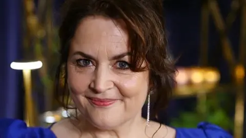 Ruth Jones, wearing a blue ballgown, smiles at the camera.