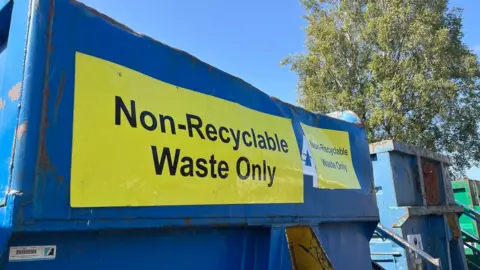 A large black and yellow sign saying Non-Recyclable Waste Only on a blue metal container at a recycling centre