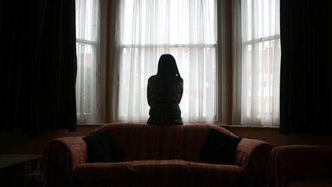 The silhouette of a woman standing alone in front of a window in a dark room