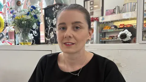 A woman in a black top sits in a cafe looking at the camera.