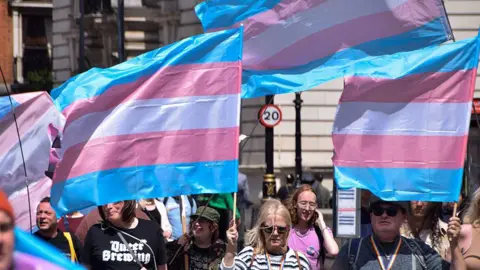 Getty Images Protesters march with trans pride flags in Whitehall during a demonstration in support of trans rights, following the Supreme Court ruling that the definition of a woman is based on biological sex. 