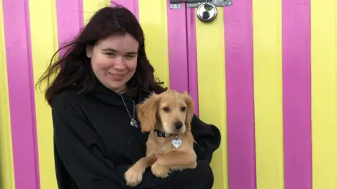 Pete Aitken Hannah standing with her puppy in front of a beach hut 