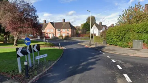 Roundabout with road sign and house in the sunshine in the distance