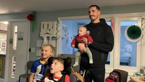 Captain Lewis Dunk holding a baby and posing for the camera with two older children, one wearing a football kit