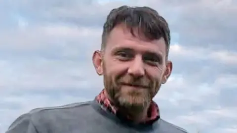 Jim Mair - a man with dark hair and a beard, smiling into the camera