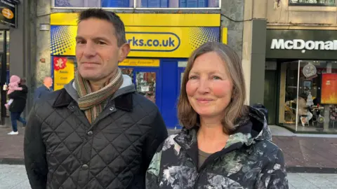 John and Helen Chandrinos smiling at the camera on a high street in Cardiff