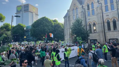 Crowds walking with a banner saying 'United for Grenfell'. In the background is Grenfell Tower