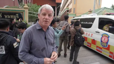 Correspondent Jonathan Head outside school as ambulance drives off on his right