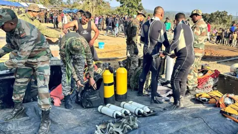 Defense PRO, personel tentara India Guwahati dengan beberapa di antaranya mengenakan pakaian penyelam, dengan peralatan seperti tabung gas berwarna kuning dan putih, tali dan jaket pelampung tergeletak di mana-mana.