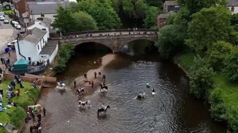 People and horses in the river at the Appleby Horse Fair, the annual gathering of gypsies and travellers in Appleby, Cumbria