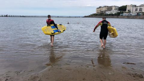 Two RNLI lifeguards with surfboards in the water 