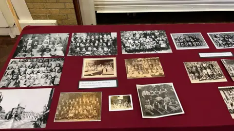 A selection of black and white photographs of school children laid out on a red table cloth