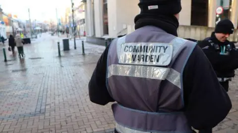 North Lincolnshire Council The back of a litter enforcement officer with a purple high-vis vest saying 'community warden' in Scunthorpe town centre 
