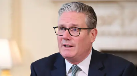 Sir Keir Starmer pictured in Downing Street, wearing a suit, white shirt and blue tie, as well as his black-rimmed glasses