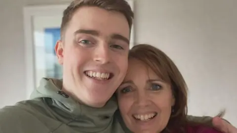 Family handout A young man with brown hair smiling with his arm round a woman, his mum.