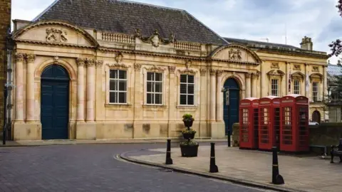 Single-storey stone-built county hall building with telephone boxes in foreground