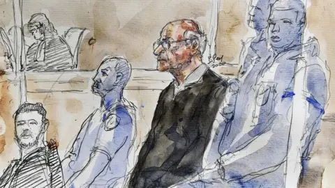 The AFP Court of AFP Joel Le Skorank is showing his trial on charges of rape and sexual assault of four children in the court in the saint, west of France in 2020. Le Scouarnec wears a dark suit. He wears glasses and fixes white hair on the back of his head. 