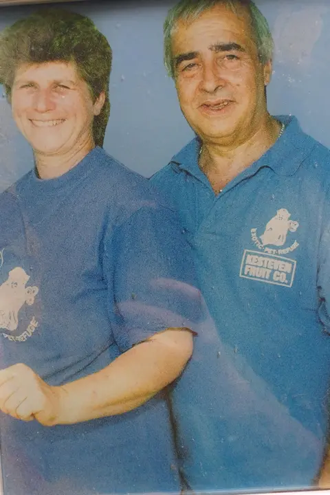 Pam Mansfield A couple, then in their 50s, smile for the camera. They are wearing blue T shirts with Exotic Pet Refuge badges on the front. 