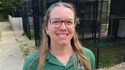 Hannah Hall, Wildlife Coordinator at Folly Wildlife Rescue, stands next to aviary with a buzzard enclosed
