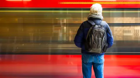 A senior man waiting outdoors on a train station platform.